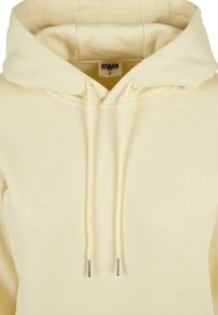 Sweat à capuche beige avec cordons et étiquette de marque Urban Classics visible en taille XS à l'intérieur de la capuche.