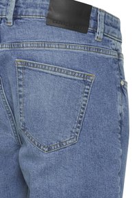 Lyseblå denimjeans med en standard baklomme, en svart lærmerkelapp i midjen og kontrasterende sømmer.