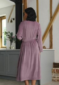 Pikk, maasika värvi mantel pehmest, tekstureeritud kangast, millel on pikad varrukad ja vöökoht. Lihtne disain, sääre keskosa pikkus.