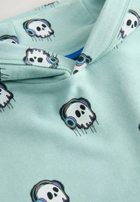Sudadera de color azul claro con un estampado general de calaveras estilizadas usando auriculares. El material es suave y tiene una textura lisa.