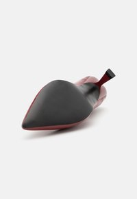 High-heeled shoe with a pointed toe design, featuring a glossy red upper and a matte black rubber sole with textured patterns.