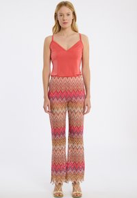 Koraalrode spaghettitop met V-hals, gecombineerd met een patroon van wijde broek met zigzagontwerpen in bruin, roze en paars en gegolfde zoom.