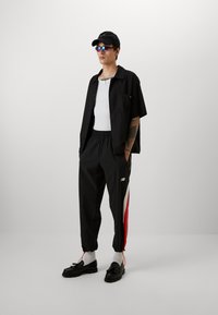 Black button-up shirt, white tank top, black joggers with red side stripes, black shoes, white socks, black cap, and blue sunglasses.