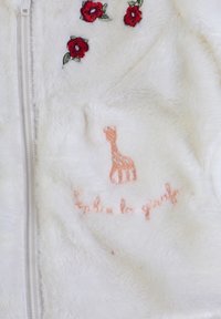 Giacca zip-up bianca pelosa con ricami floreali rossi e un design di giraffa color pesca. Morbida al tatto, con una cerniera liscia.