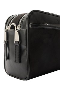 Czarna skórzana torba o gładkiej fakturze, wyposażona w srebrne okucia i podwójne zamki błyskawiczne. Dodatki obejmują skórzane uchwyty zamków i wyraźnie zarysowany kształt.