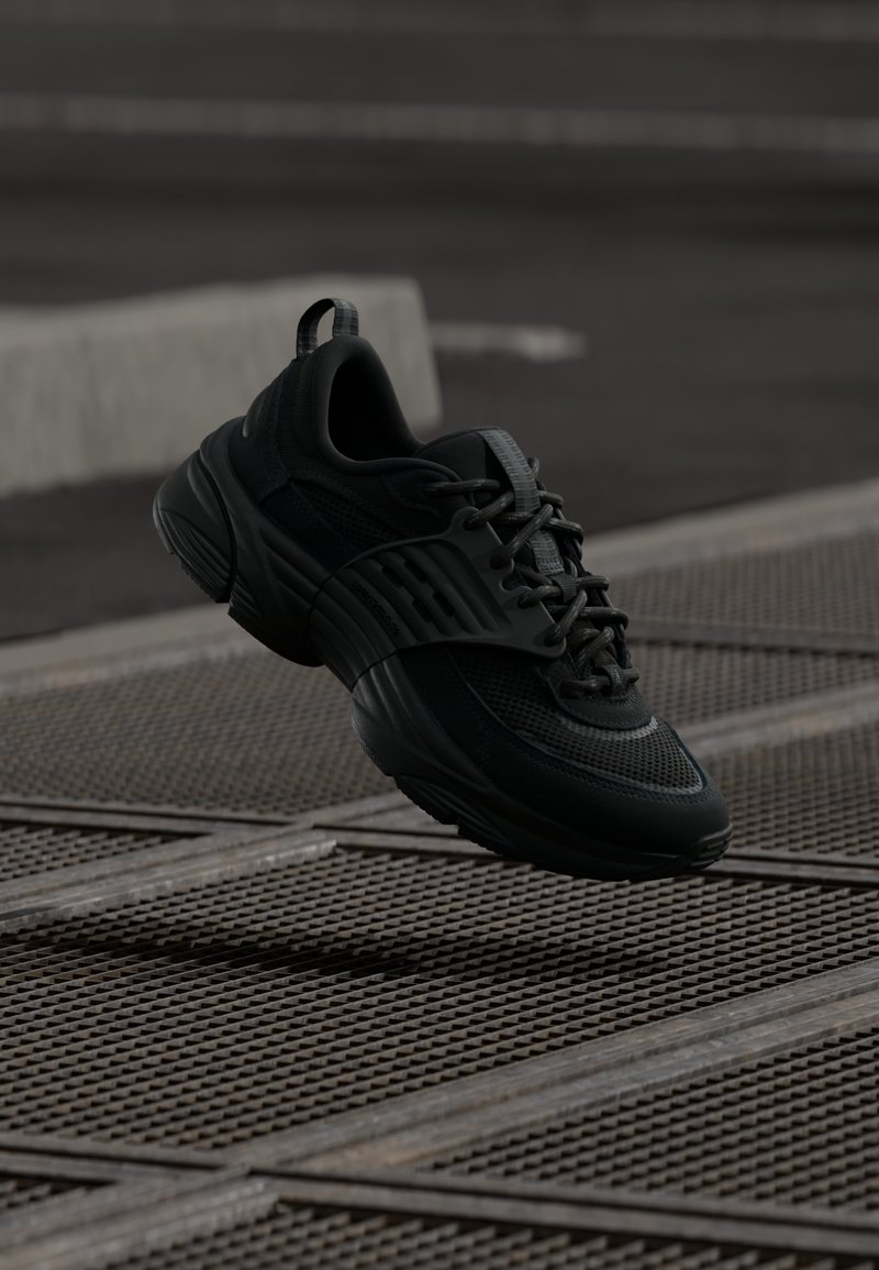 Czarne buty sportowe z teksturowaną siateczką i gumową podeszwą, charakteryzujące się grubą sylwetką i systemem sznurowania zapewniającym pewne dopasowanie.