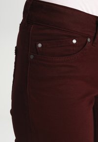 Burgundy jeans har en figurnära design med silverfärgad hårdvara, fem fickor och subtila sömnadsdetaljer för extra textur.