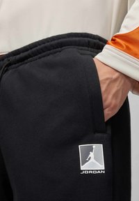 Zwarte sweatpants van zacht materiaal, met een witte Jordan-logo op de linkerzak. Elastische tailleband met een gedetailleerd zakontwerp.
