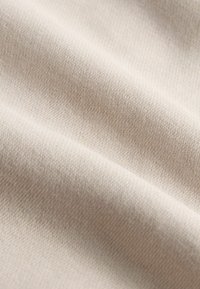 Lichtbeige stof met een gladde textuur en een subtiel geweven patroon, zichtbaar met plooien en vouwen voor diepte.