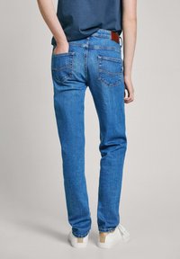 Blå denimjeans med rak passform, synlig sömnad och två bakfickor. Bärs med vita sneakers och en blå skjorta.