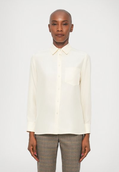 Chemise à boutons couleur crème clair avec un col, des manches longues et une poche poitrine, portée avec un pantalon slim à motifs.