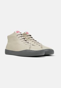 Zapatos de tobillo de cuero beige con suelas de goma grises, que presentan una punta redondeada, acentos de hilo y un logotipo rojo en la lengüeta.