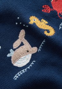 Tissu tricoté avec dauphin beige brodé, hippocampe jaune et crabe rouge partiel sur fond bleu foncé avec bulles blanches cousues.
