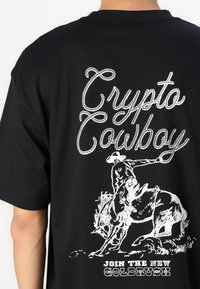 Sort t-shirt med hvidt trykt tekst "Crypto Cowboy" og en cowboy-illustration. Blødt bomuldsstof, korte ærmer, afslappet pasform.
