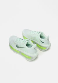 Pantofi de alergare Nike verde deschis, cu un superior din plasă, dotati cu amortizare vizibilă, șireturi plate și un logo argintiu pe lateral.