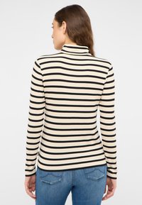 Schwarz-weiß gestreiftes Langarm-Top mit Rollkragen, gerippten Textur und figurbetontem Schnitt, getragen mit blauen Jeans.