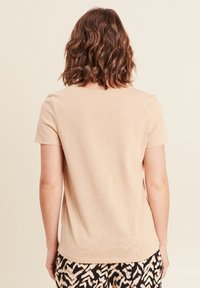 Beige T-shirt met korte mouwen en ronde hals, zachte textuur en een comfortabele pasvorm, gecombineerd met gemusterde zwart en crèmekleurige broek.