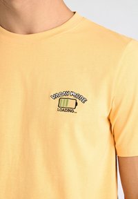 Camiseta amarilla de manga corta hecha de algodón, con un diseño bordado de un ícono de batería y el texto "CARGANDO MODO VACACIONES...".