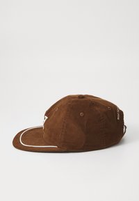 Brown corduroy cap with a curved brim, white accent stitching, and adjustable strap. Features ventilation holes and embroidered logo.