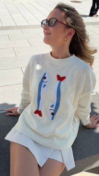 Sweter w kolorze kremowym, wykonany na drutach, z motywami dwóch ryb w kolorach niebieskim i czerwonym, z prążkowanymi mankietami i okrągłym dekoltem.