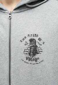 Γκρι φούτερ με φερμουάρ, με μαύρο σχέδιο χαρακτήρα πανκ και κείμενο που προωθεί την εκδήλωση "The Litter Box" με διεύθυνση και προσφορά μπύρας $5 κάθε Παρασκευή.