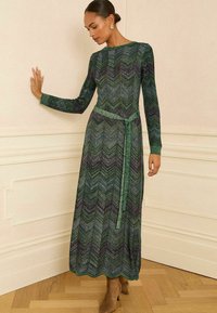 Pikkade varrukatega roheline kleit, millel on liblikakujuline muster, rõhutatud vöökohaga ja tekstuurse kangaga. Kleeit on kaunistatud sobiva vöödiga.