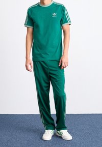 Grön bomullströja med grå detaljer, korta ärmar och en liten logotyp. Matchas med gröna träningsbyxor med sidremsor.