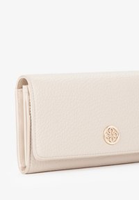 Beige lederen portemonnee met een gestructureerde afwerking, een overslagontwerp en een gouden embleemdetail aan de voorkant. Compacte en rechthoekige vorm.