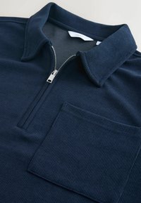 Polo shirt a coste blu navy con zip argentata, colletto a punta e taschino rettangolare sul petto.