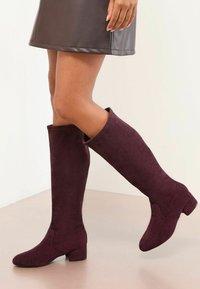 Burgundy velúr térd fölé érő csizmák sima textúrával, kerek orral és tömbsarkúval. Egyszerű dizájnnal rendelkezik, látható hardver nélkül.