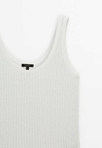 Hvid ribbet tanktop med rund halsudskæring, lavet af et let, tekstureret stof. Har en mærkat nær midten.