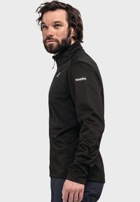 Schwarzer Fleece-Pullover mit hohem Kragen und langen Ärmeln. Mit einem Logo auf dem oberen Ärmel. Glatte Textur und taillierte Passform.