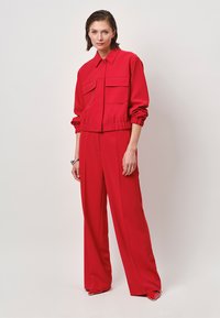 Rode polyester jas met twee voordo pockets, elastische tailleband en bijpassende hoge taillebroek, met een losse, vloeiende vorm.