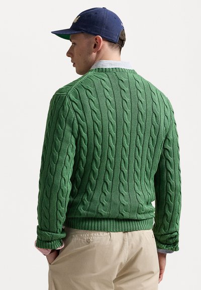 Green cable-knit sweater with ribbed hem and cuffs, featuring a textured pattern. Worn over a light blue collared shirt.