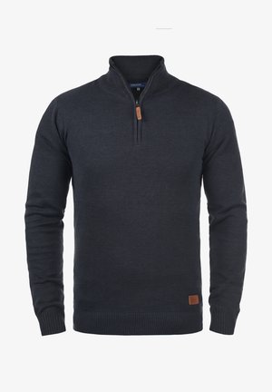 Marineblå strikkegenser med halv glidelås, ribbestrikkede mansjetter og nederkant, samt et lite skinnlogo-patch på venstre nederste hjørne.