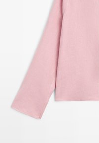 Lange mouw van een lichtroze katoenen overhemd afgebeeld tegen een witte achtergrond, gericht op stiksels en de textuur van de stof.