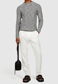 Grå strukturerad långärmad tröja, vita lätta byxor, svarta platta sandaler och en liten svart korsväska. Minimalistisk design, avslappnad passform.