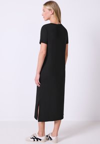 Mustapitsin maxi-mekko, jossa on lyhyet hihat ja pehmeä kangas. Siinä on sivuhalkio liikkumisen helpottamiseksi, yhdistettynä valkoisiin lenkkareihin.