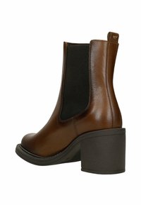Hnědé kožené kotníkové boty s černým elastickým bočním panelem a masivním blokovým podpatkem na bílém pozadí.