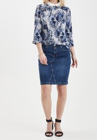 Bloemmotief lange mouwen top in navy en grijs, gecombineerd met een donkere denim kokerrok. Zwarte haksandalen complementeren de outfit.