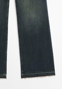 Ciemnoniebieskie dżinsy z prostą nogawką i postrzępionymi zakończeniami na białym tle.