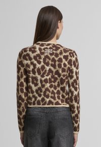 Hnedý a béžový sveter s leopardím vzorom, zaobleným výstrihom, dlhými rukávmi a rebrovaným lemom. Mäkká textúra a štítok viditeľný na zadnej strane.