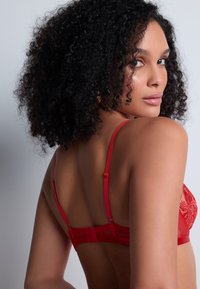 Soutien-gorge en dentelle rouge avec un dos en maille transparente et des bretelles ajustables. Broderies florales sur les bonnets et fermeture à crochets sur la bande.