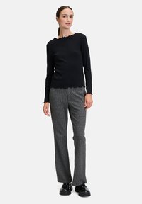 Czarny longsleeve z falbaniastym dekoltem, zestawiony z szarymi, teksturowanymi spodniami i czarnymi butami na platformie.