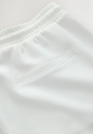 Pantaloni albi din țesătură texturată cu talie elastică și buzunar posterior orizontal cu deschidere, prezentate în prim-plan detaliat.