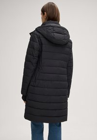 Zwarte gewatteerde jas met capuchon, met een doorgestikt ontwerp, elastische manchetten en een halflange snit, gestyled met een blauwe spijkerbroek.