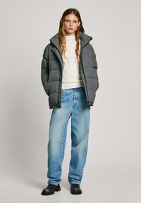 Šedá péřová bunda s vysokým límcem, bílý žebrovaný svetr a volné světle modré džíny. Černé kotníkové boty dotvářejí outfit.