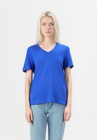 Blå V-hals t-skjorte laget av mykklede, med korte ermer og avslappet passform, kombinert med lyseblå jeans.