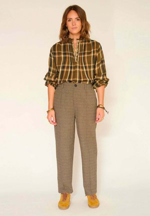 Chemise à carreaux en vert, jaune et marron ; pantalon à carreaux taille haute ; chaussures jaune moutarde. Tissus texturés.