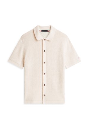 Camisa beige de manga corta con botones y cuello, tela texturizada y pequeño logo en la manga izquierda.